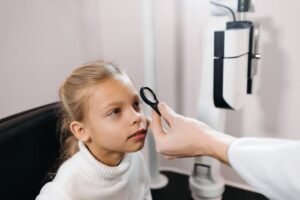 A young girl sitting in an ophthalmologist's office having her eyes examined.