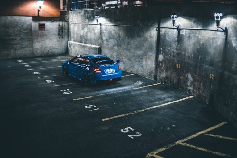 A blue car parked at night in a dimly lit urban parking lot with numbered space markings.