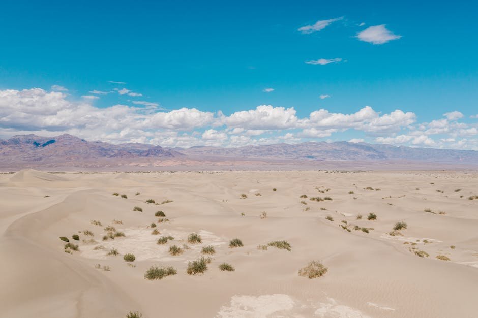 Expansive desert dunes under a clear blue sky with white clouds in Death Valley.