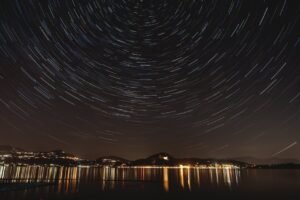 A mesmerizing long-exposure photo capturing star trails above a serene lakefront at night.