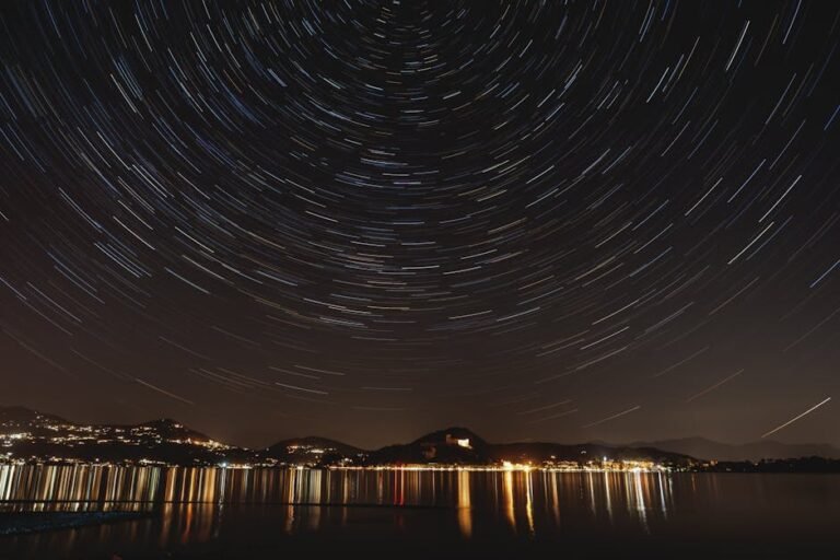 A mesmerizing long-exposure photo capturing star trails above a serene lakefront at night.