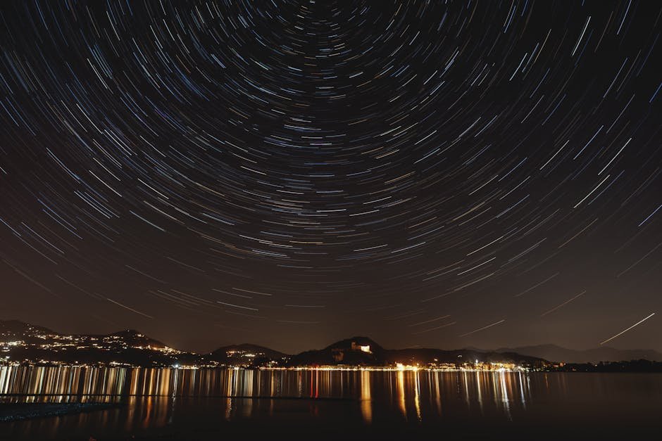 A mesmerizing long-exposure photo capturing star trails above a serene lakefront at night.
