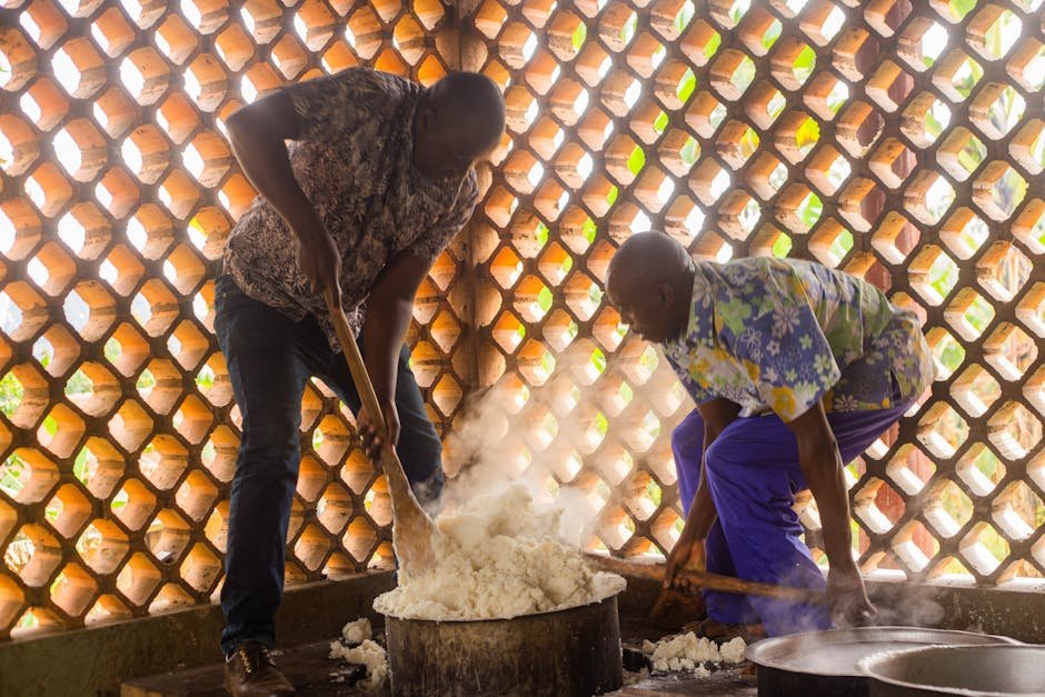 Two African men cook a traditional meal in a uniquely designed indoor space with natural light patterns.