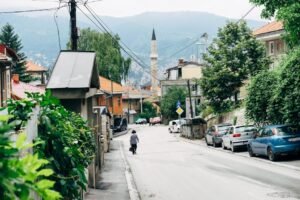 A typical Sarajevo street scene with a mosque minaret and cars parked along the road.