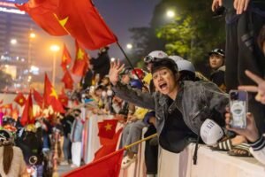 Joyful crowd celebrating with Vietnamese flags at night in Hanoi, Vietnam.