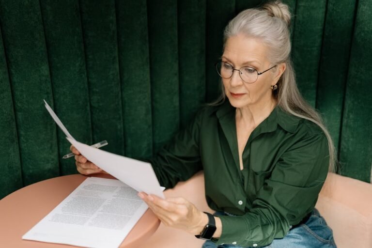 Senior woman wearing glasses, reading documents at a desk indoors, showcasing professional focus.