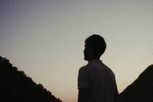 Silhouette of a man against twilight sky, framed by mountains, creating a serene and contemplative atmosphere.