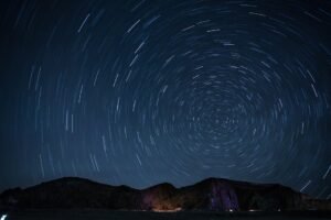 A mesmerizing night sky showcasing rotating star trails over a mountainous landscape.