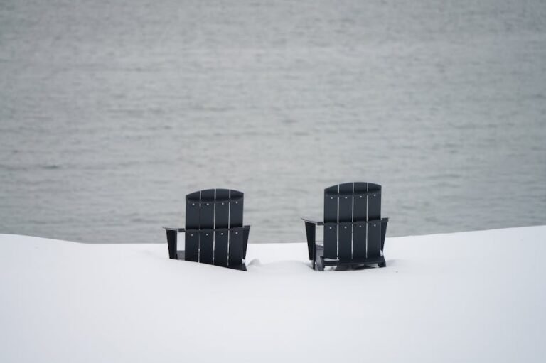Two black Adirondack chairs in a snowy landscape by a serene lake. Perfect for winter-themed imagery.