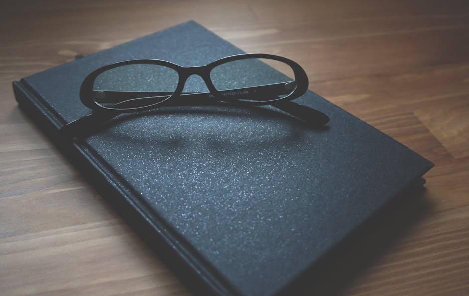 Black notebook with eyeglasses on a wooden surface, capturing a professional and classic vibe.