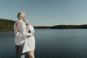 A senior couple sharing a loving embrace by a serene lakeside, symbolizing enduring love.