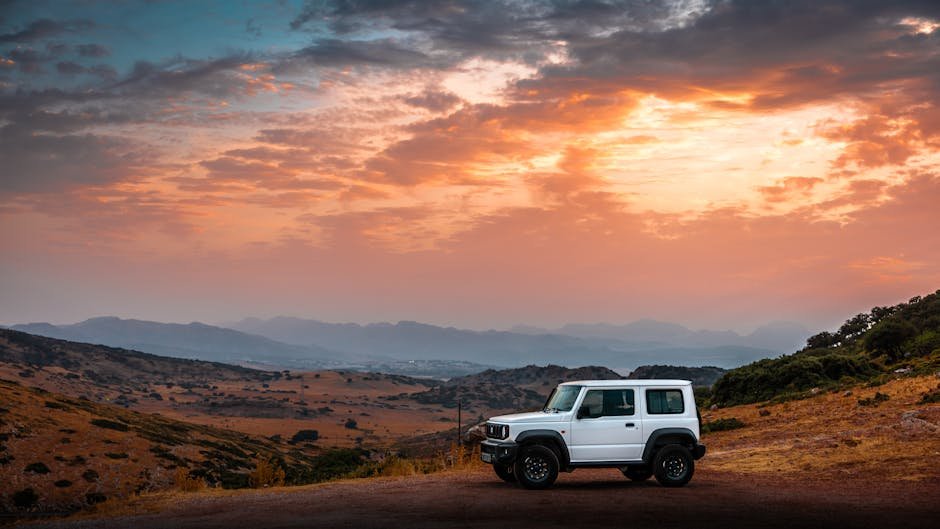A white SUV parked in a scenic mountainous landscape under a vibrant sunset sky.