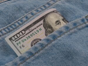 Close-up of a 100 dollar bill peeking from a blue denim pocket, symbolizing wealth and finance.